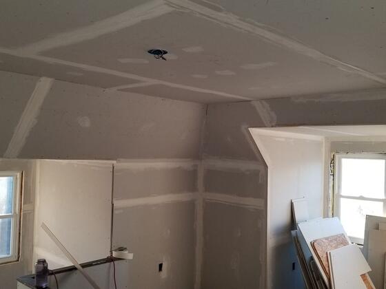 New drywall around a pair of dormer windows, with spare sheets on the floor