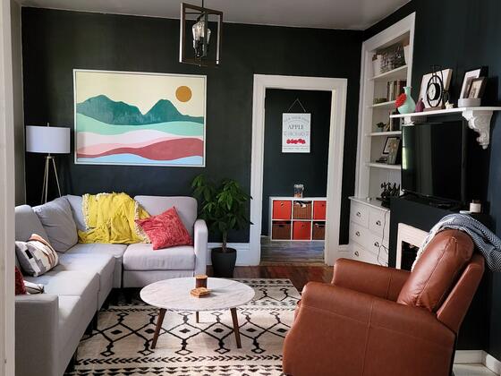 A living room with dark green walls, a gray sofa, and a brown leather armchair