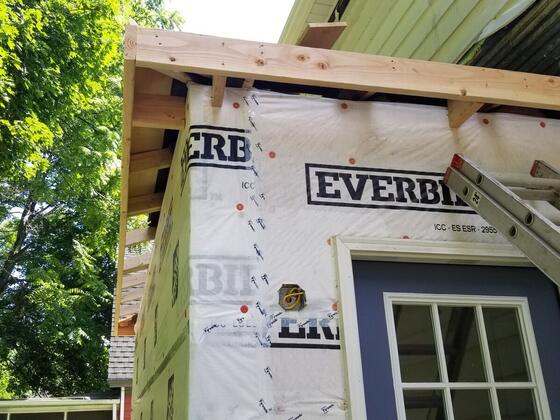 A new rear addition wrapped in house wrap, with a framed window and a ladder against the wall