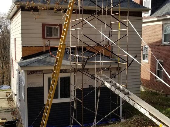 Scaffolding against the back of the house while new dark siding goes on the addition